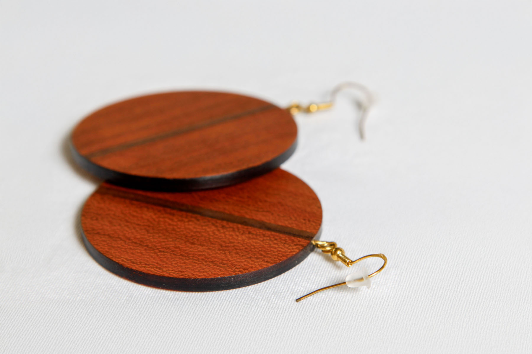 Runde Ohrringe aus Holz mit goldfarbenen Haken liegen auf weißem Stoff.